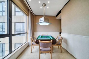 Una habitación con mesa de billar, cuatro sillas, una lámpara en el techo y ventanas amplias.