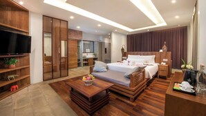 A modern hotel room with a large bed, a flat-screen TV, wooden furniture, and a dining area. - Siemreap Vasinh Residence (Siem Reap)