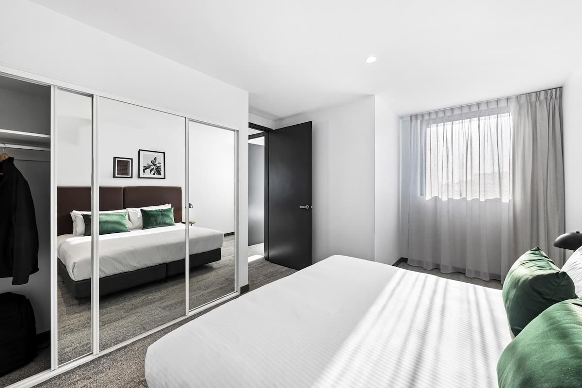 A modern hotel room with a large bed, a wardrobe with a mirror, and a view of the sea through the window.
