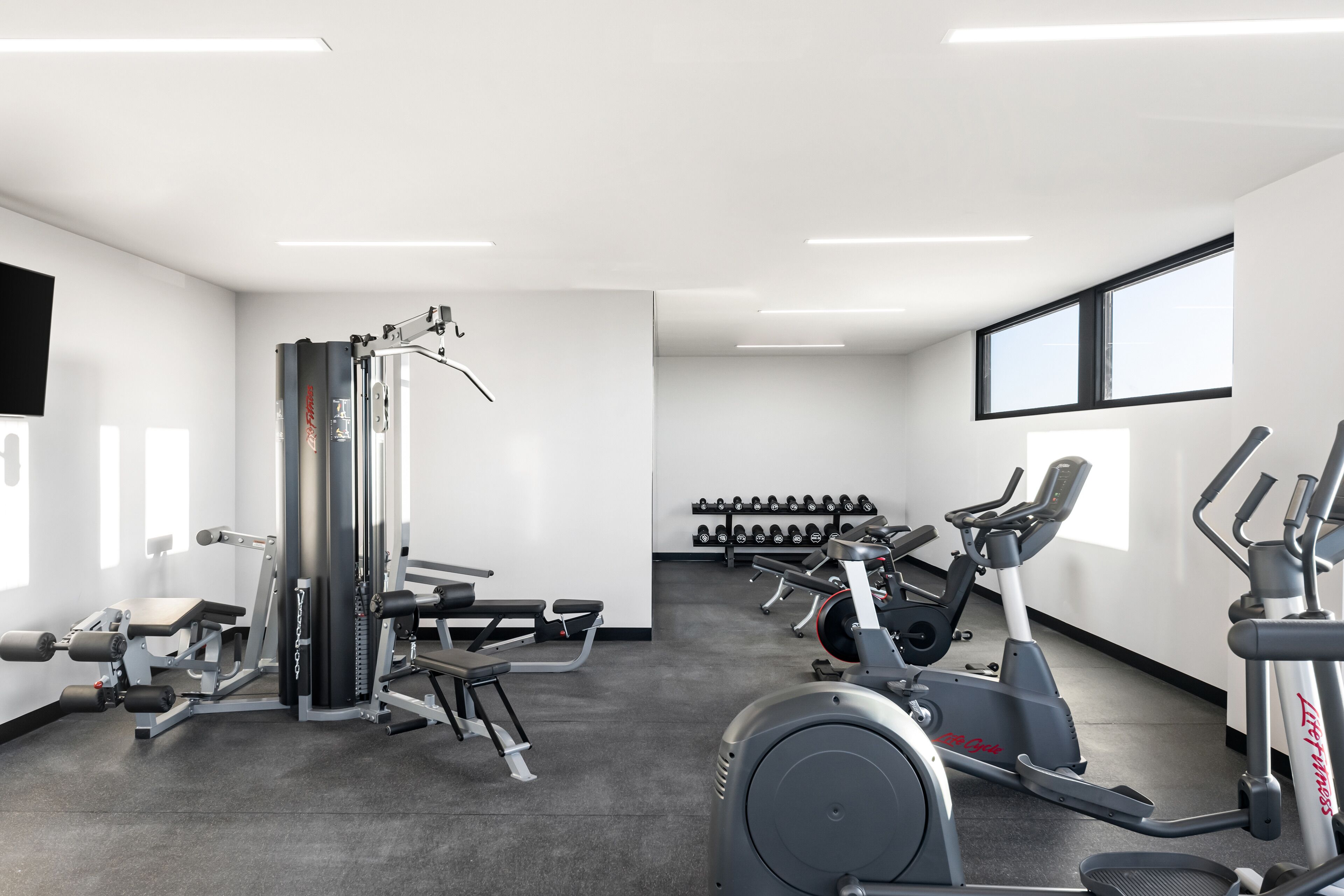 Une salle de sport équipée de divers appareils d’exercice, notamment des tapis de course et des appareils de musculation, ainsi qu’un porte-haltères.