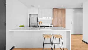 Una cocina moderna con armarios blancos, un panel de madera decorativo, un refrigerador de acero inoxidable y dos taburetes de madera.