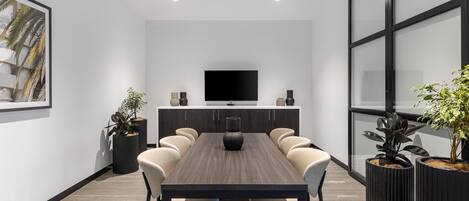A modern conference room with a long table, six chairs, a flat-screen TV, and potted plants.