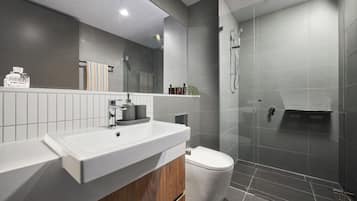 A modern bathroom with a large mirror, a white sink, a toilet, and a shower area.