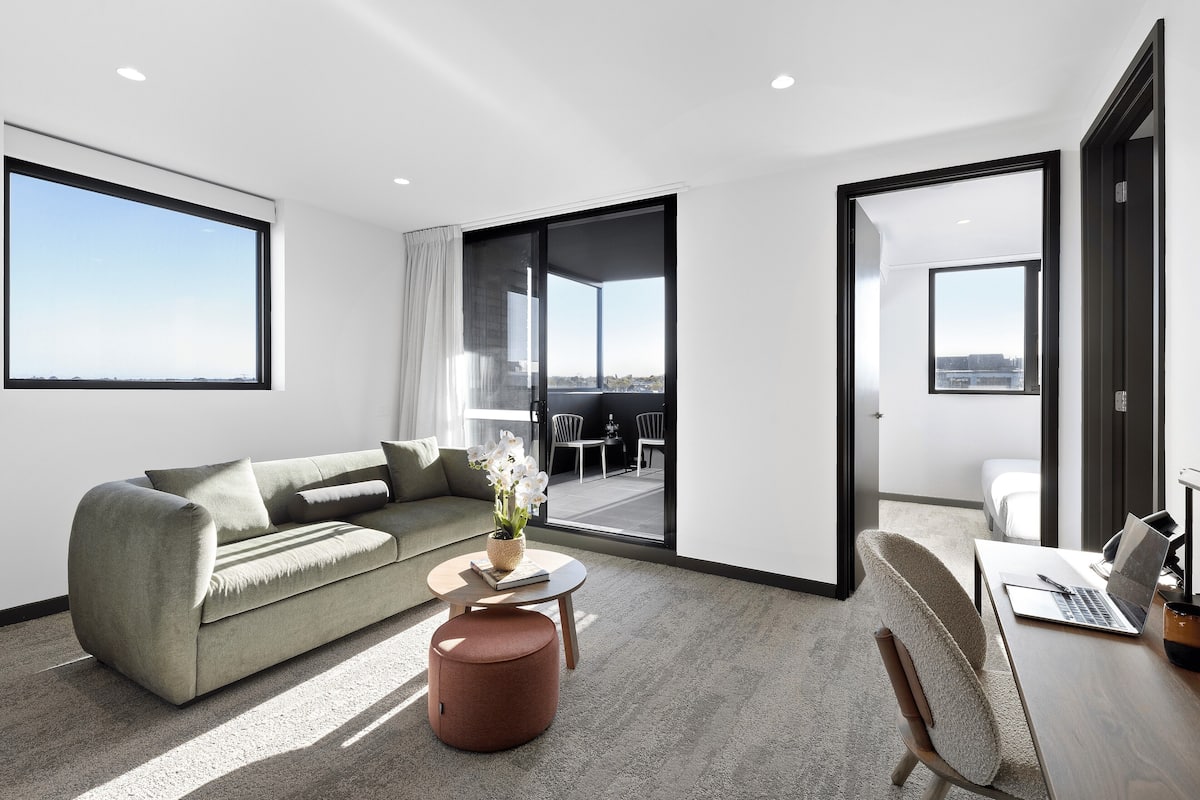 A modern living room with a sofa, a round coffee table, and a laptop on a desk.