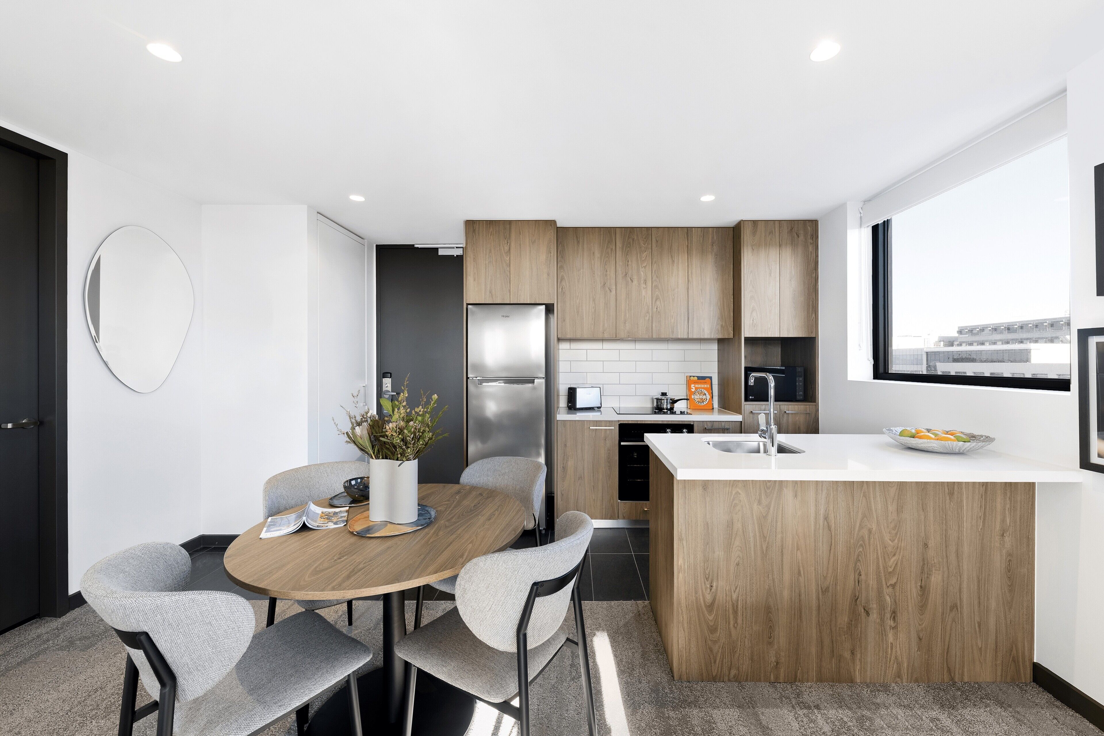 A modern kitchen with a central island, built-in appliances, and a dining area with a round table and chairs.