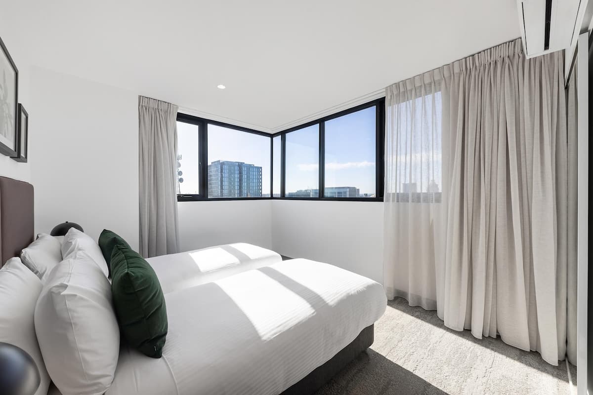 A modern hotel room with a large bed, a view of the city, and a window with sheer curtains.