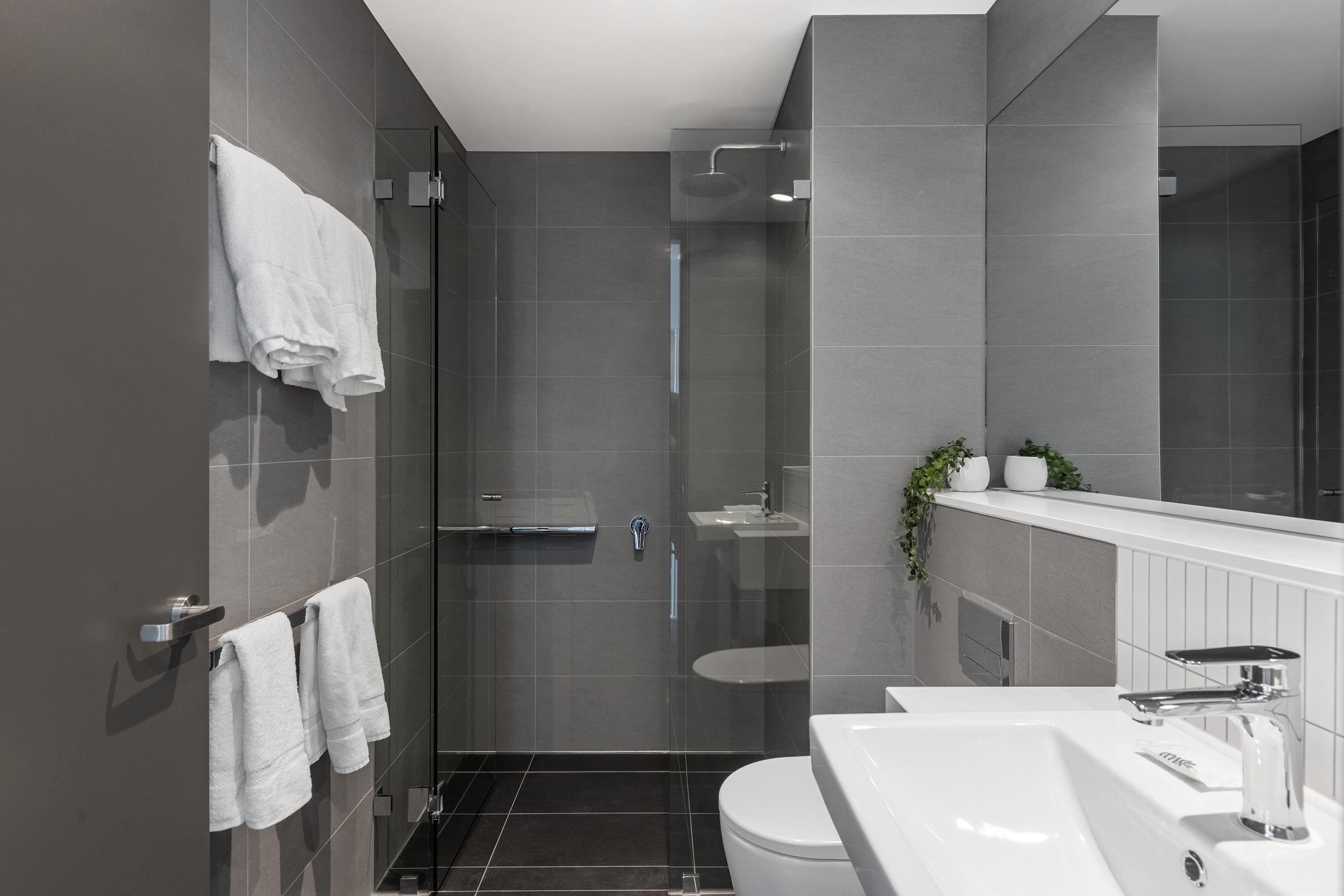 Une salle de bain moderne avec une douche à parois de verre, un lavabo blanc et un grand miroir.