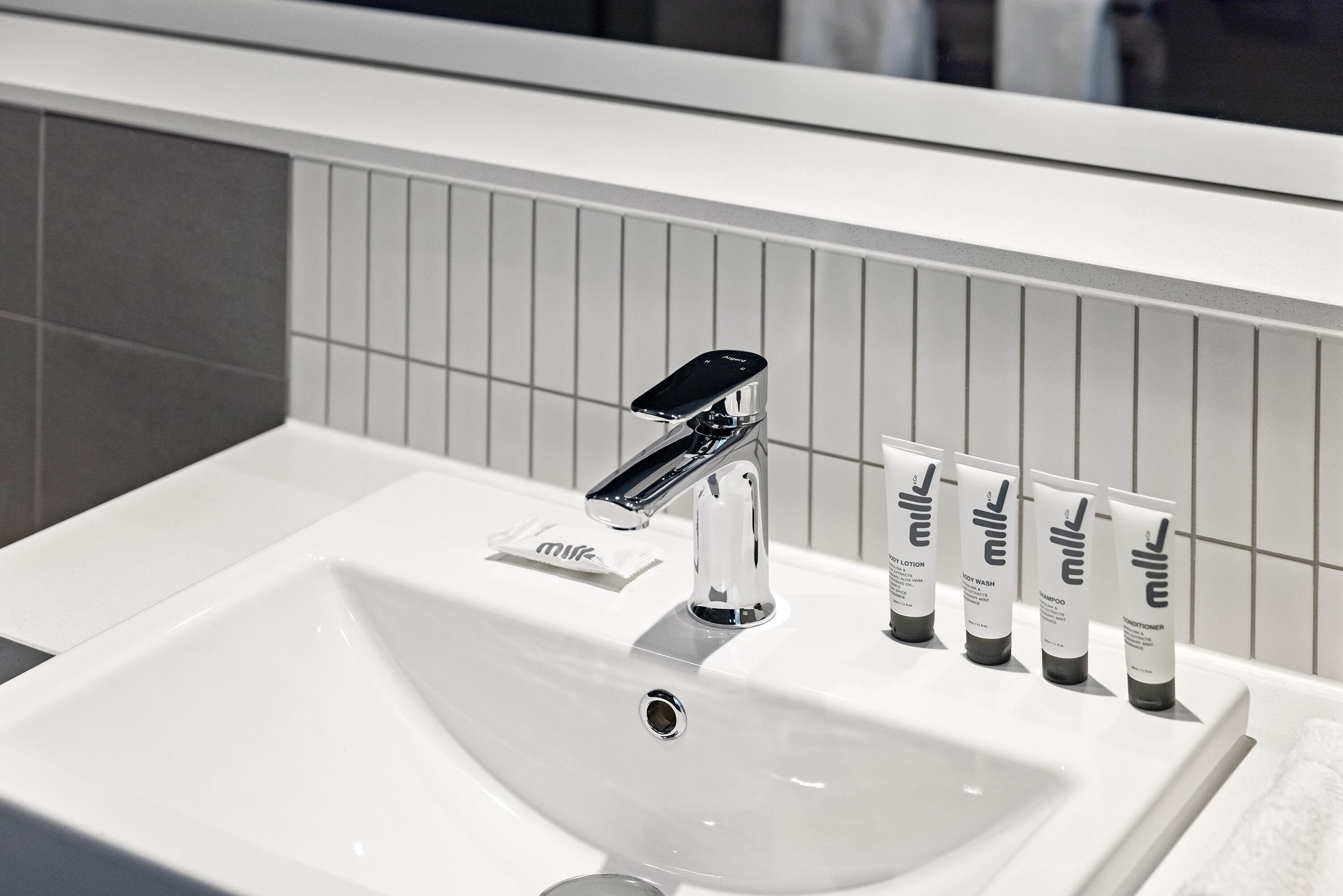 Moderni hana ja viisi tuubia maitopohjaista shampoota ja hoitoainetta kylpyhuoneen lavuaarin päällä.