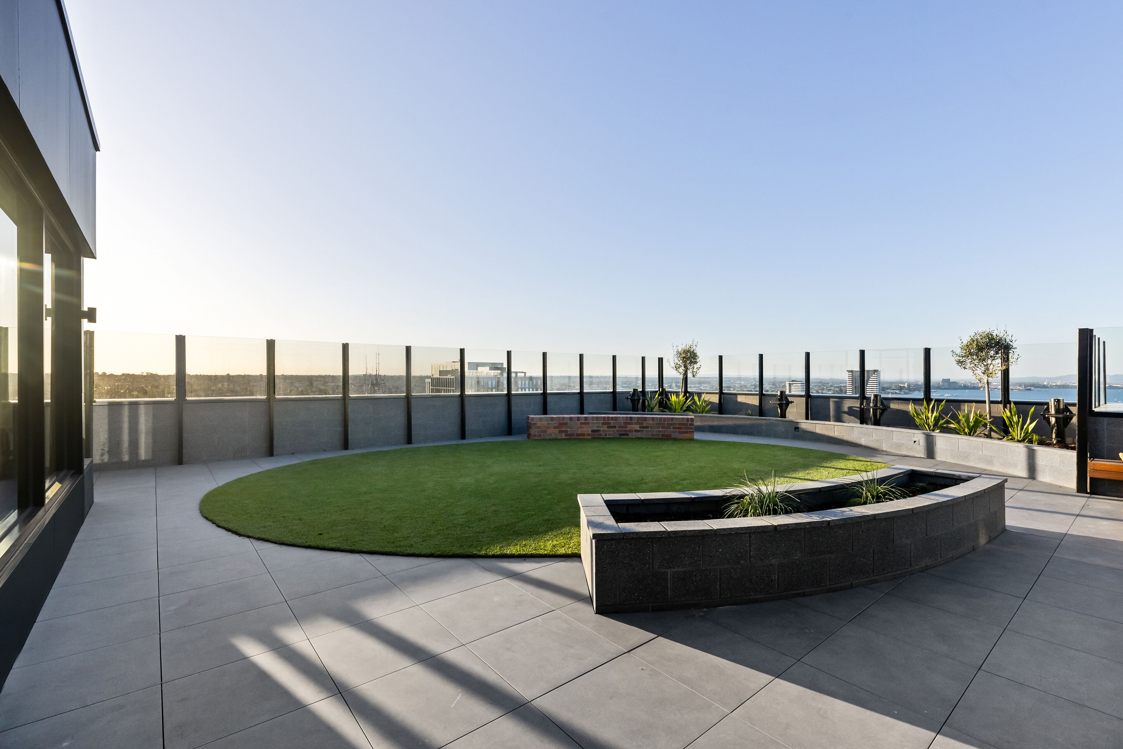 A rooftop terrace with a curved lawn, a rectangular planter, and a view of the city skyline.