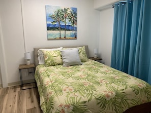 Une chambre à coucher avec un lit, deux tables de chevet, un tableau au mur et un rideau bleu.
