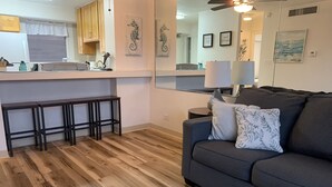 Ein modernes Wohnzimmer mit grauem Sofa, Holzböden und einer Küchenzeile mit Holzausstattung und weißer Arbeitsplatte.