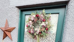 En turkosfärgad dörr med en blomsterkrans och en stjärndekoration.