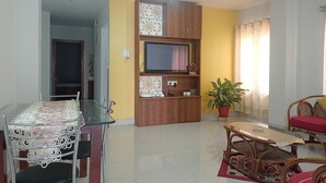 A living room with a TV, wooden cabinets, a dining table with chairs, and a potted plant. - Mi Casa (Guwahati)
