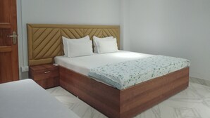 A bedroom with a wooden bed frame, two white pillows, a wooden nightstand, and a white mattress with a floral pattern. - Mi Casa (Guwahati)