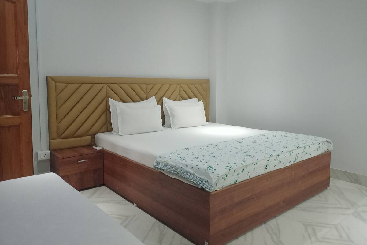 A bedroom with a wooden bed frame, two white pillows, a wooden nightstand, and a white mattress with a floral pattern.