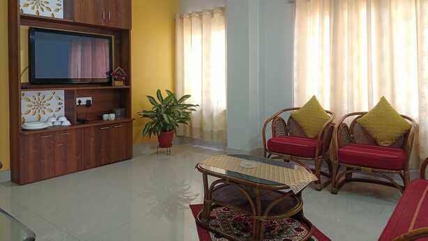 A living room with a television, wooden cabinet, potted plant, wicker chairs, and a patterned rug. - Mi Casa (Guwahati)