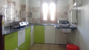 A kitchen with green and white cabinets, a built-in stove, a sink, and a window with blinds. - Mi Casa (Guwahati)