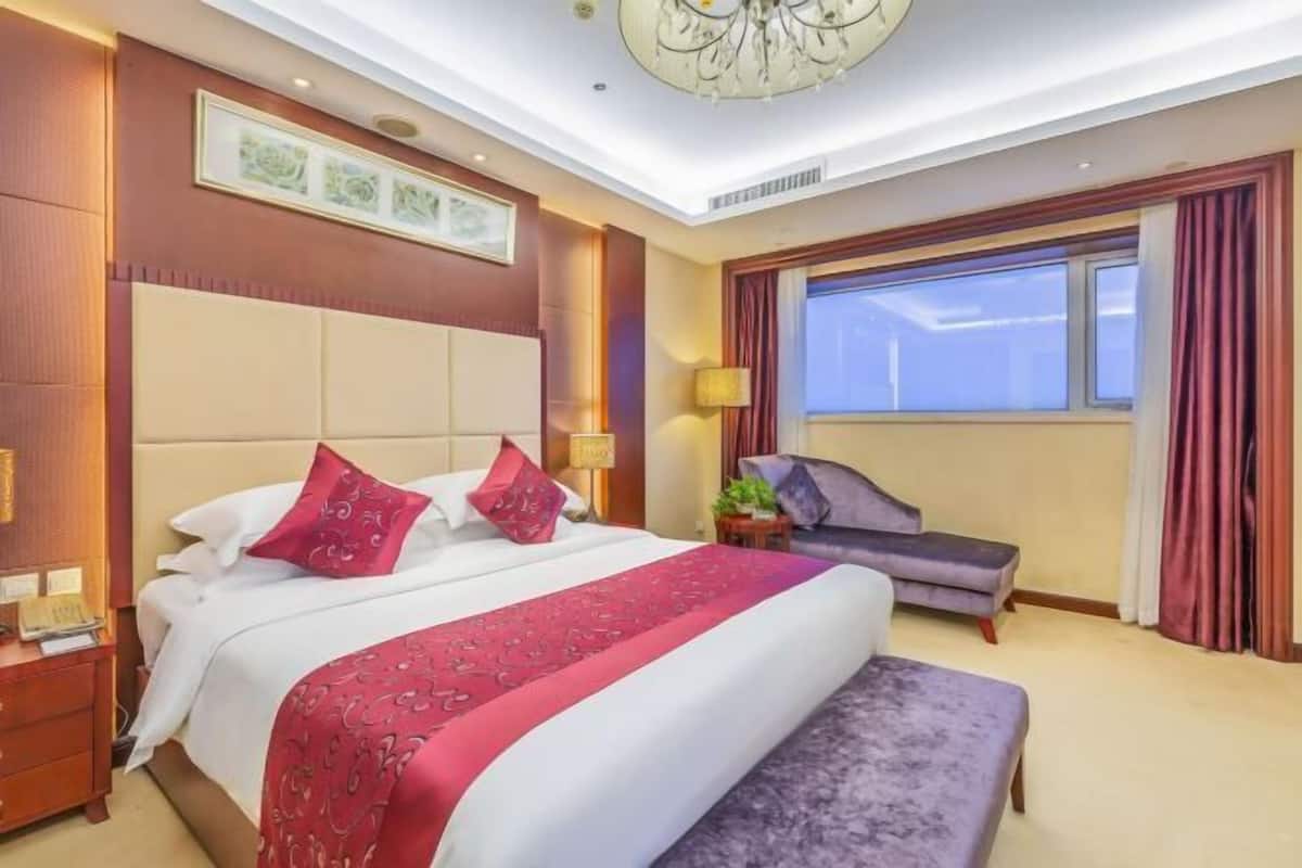 A hotel room with a large bed, a sofa, a desk, and a window with curtains.