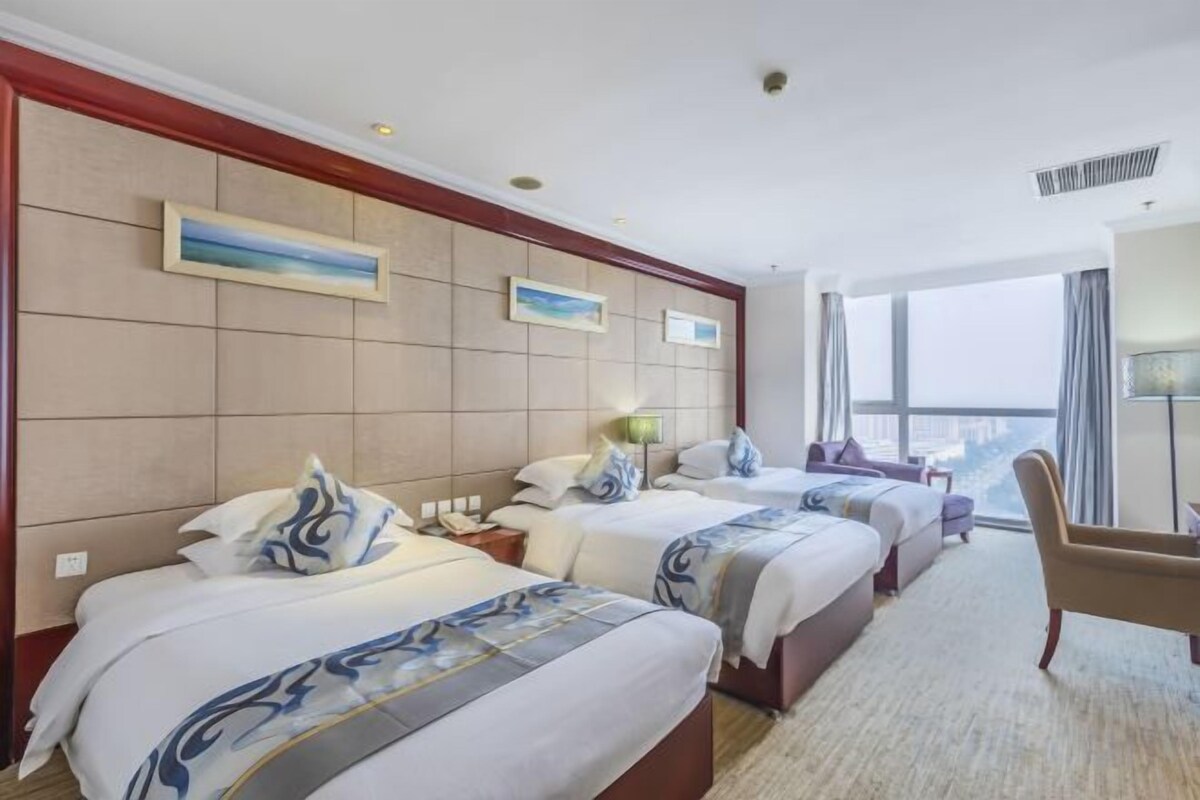 A hotel room with two beds, a sitting area, and a large window offering a city view.