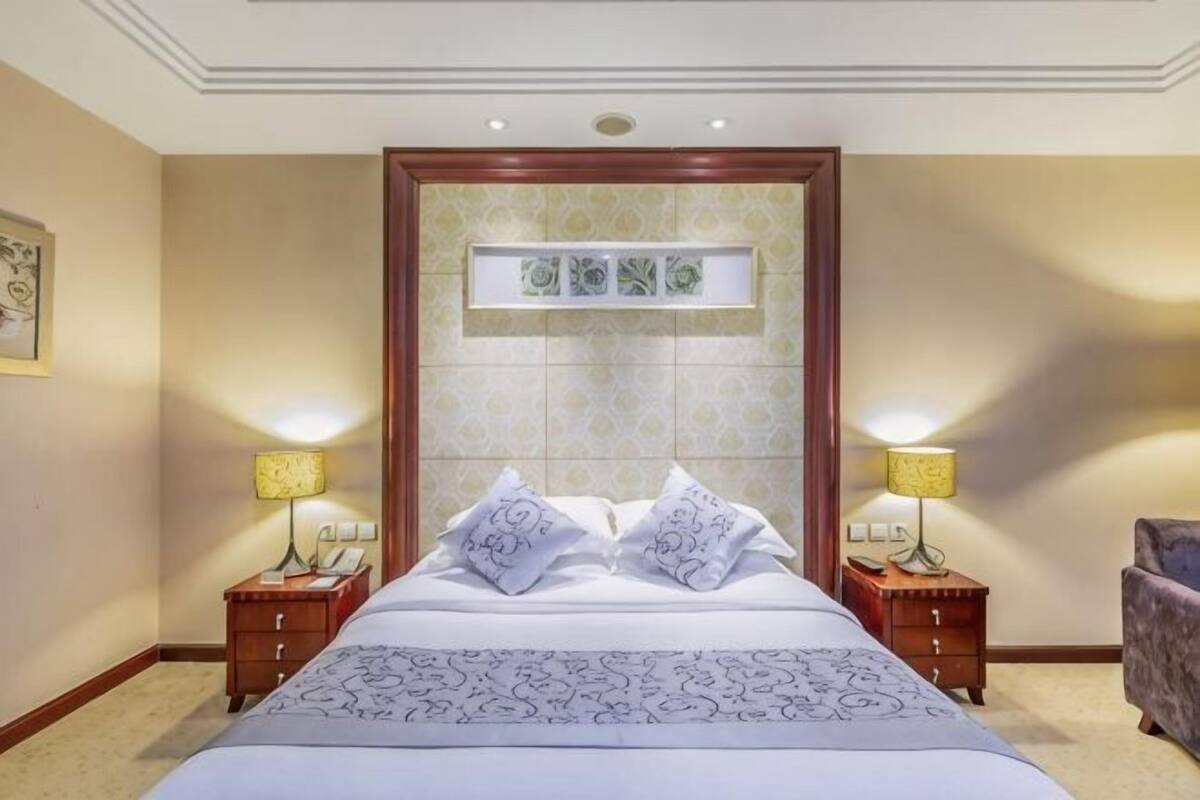 A hotel room with a large bed, two bedside tables with lamps, a small sofa, and a decorative wall panel above the bed.