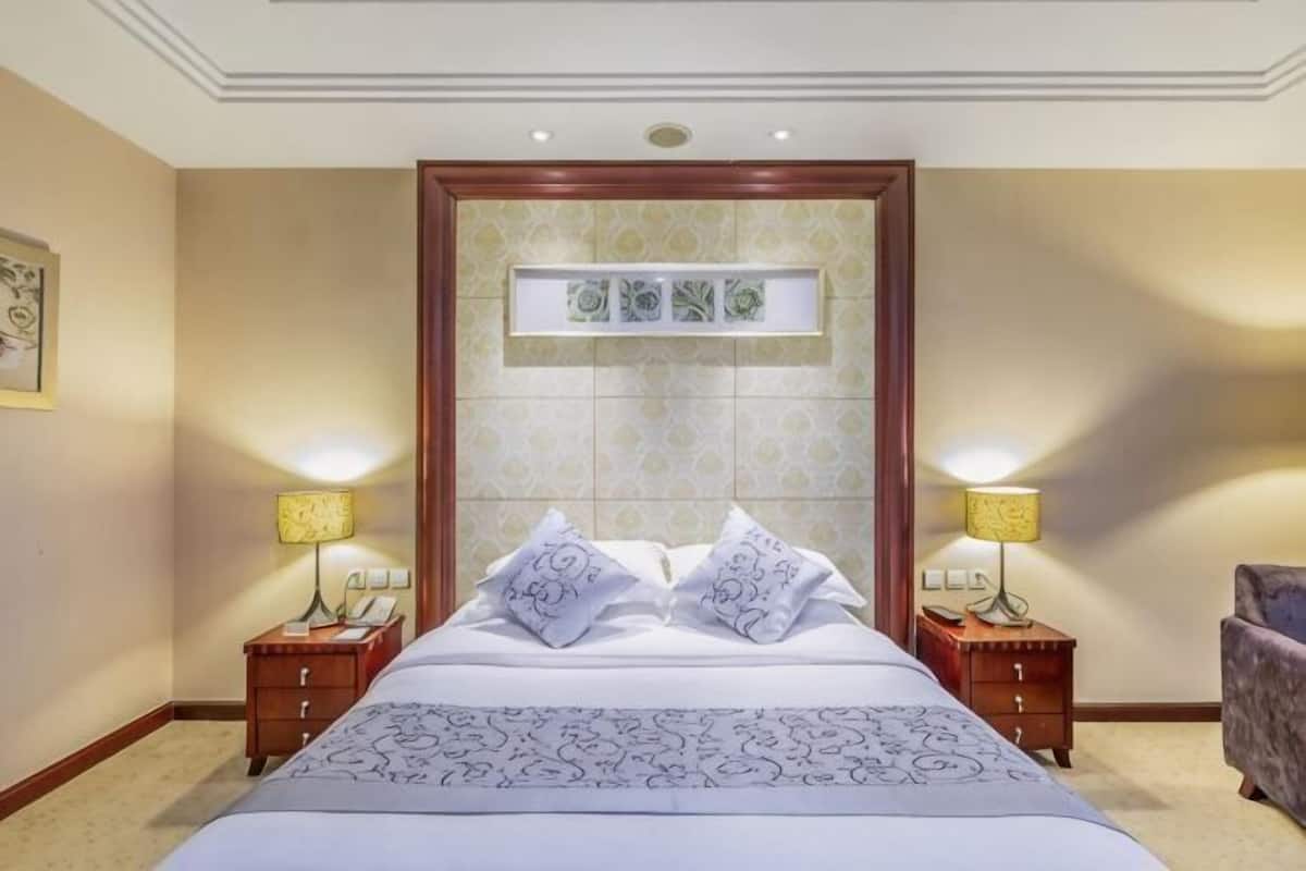 Une chambre d’hôtel avec un grand lit, deux tables de chevet avec des lampes, un petit canapé et un panneau décoratif au-dessus du lit.