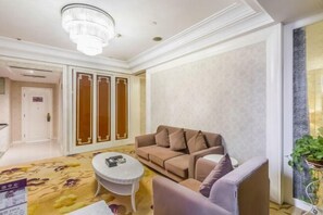 Una habitación con un sofá color beige, una mesa de centro redonda, un sillón blanco, una araña y un panel decorativo en la pared.