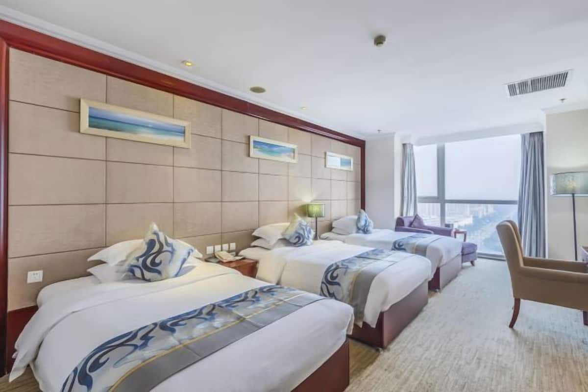 A hotel room with two beds, a sofa, a chair, and a large window offering a city view.