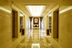 A corridor with a polished floor, a central light fixture, and a framed artwork on the wall.