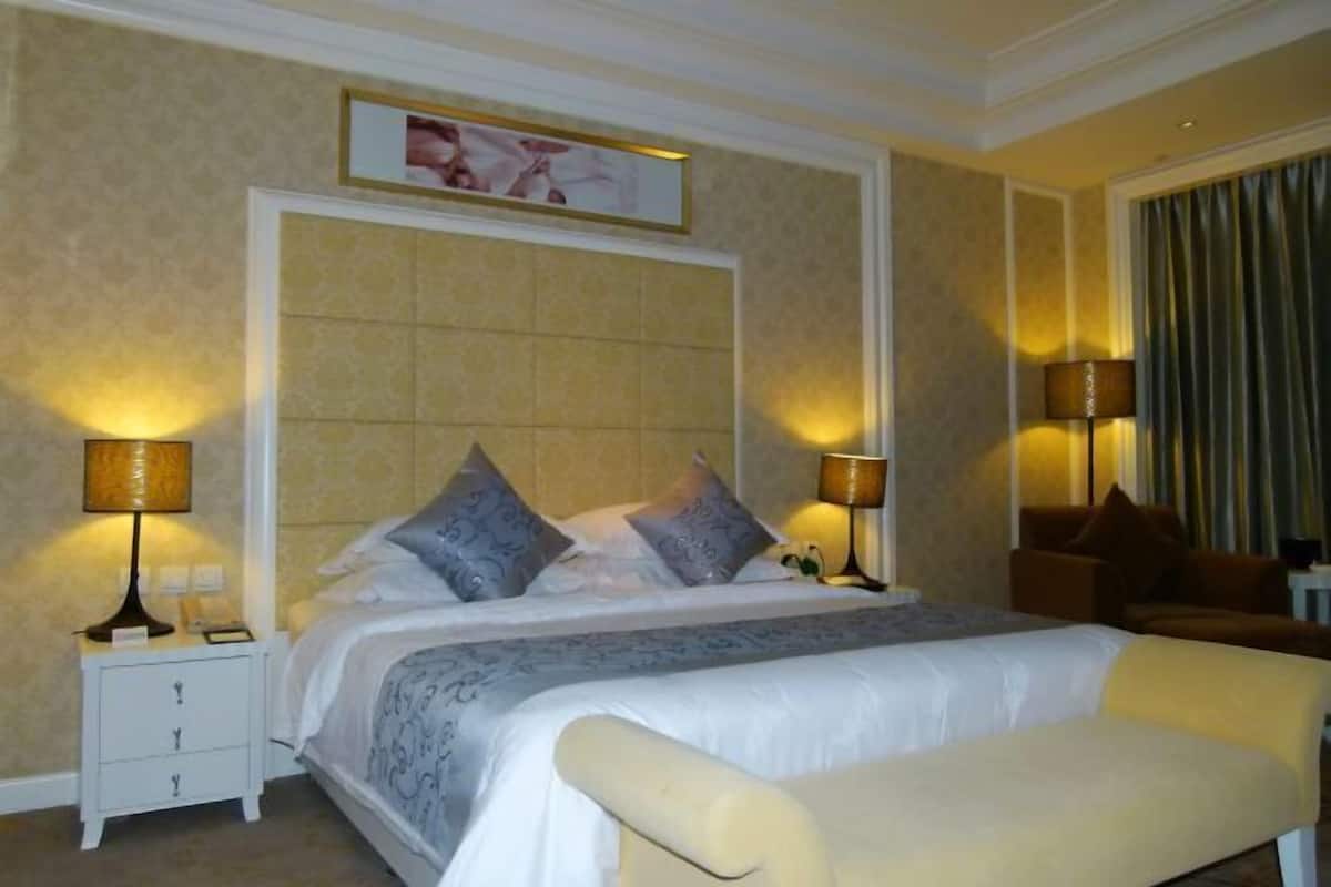 A hotel room with a large bed, two bedside tables with lamps, a chair, and a painting on the wall.