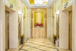 A hotel lobby with a checkered floor, a chandelier, and a wall with a golden pattern.