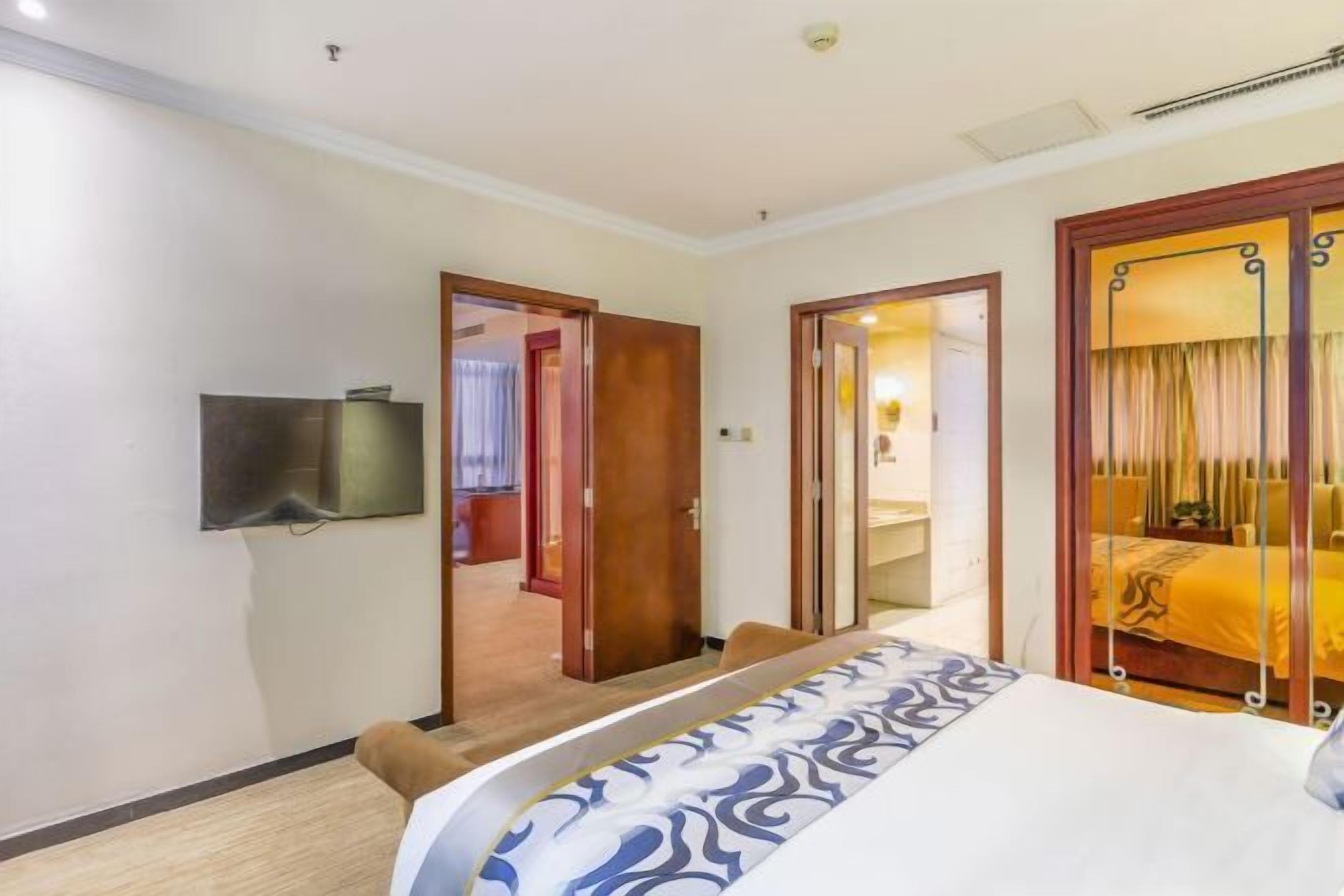 A hotel room with a bed, a TV mounted on the wall, and a door leading to another room.