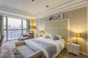 Habitación de hotel con una cama grande, un sofá, un escritorio y una silla. Se ve una ventana con vistas a edificios.