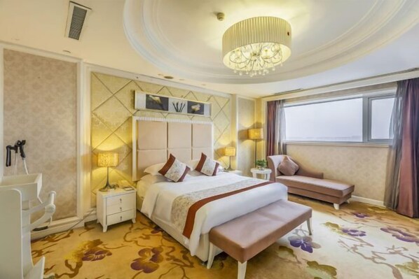 A hotel room with a large bed, a bench, a bedside table, a nightstand, a chandelier, and a window with curtains.