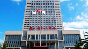 A multi-story building with a prominent entrance, a flagpole with flags, and a statue in front.