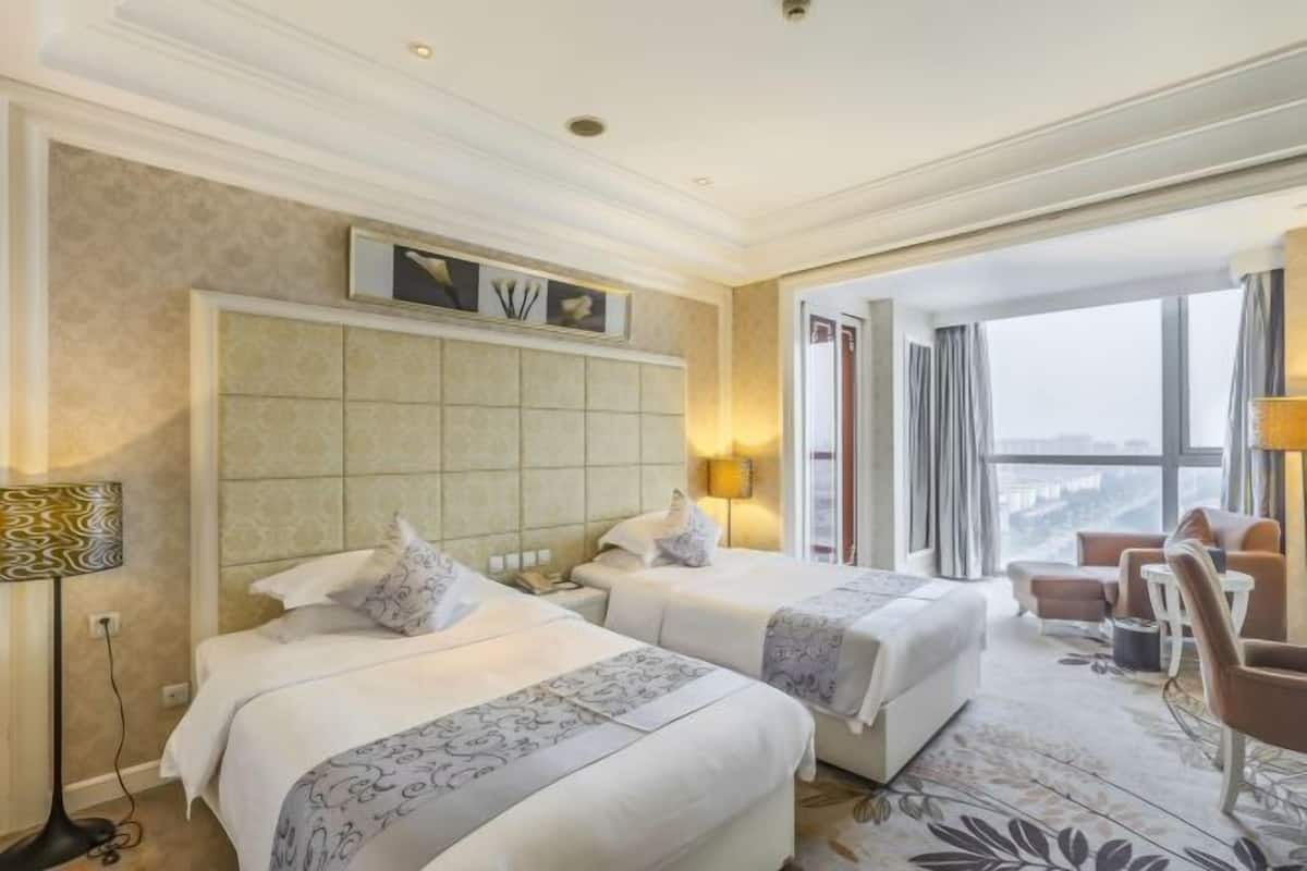 A hotel room with two beds, a large window, a sofa, and a lamp.
