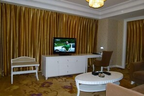 A hotel room with a television on a white cabinet, a small white chair, a brown armchair, and a round coffee table.