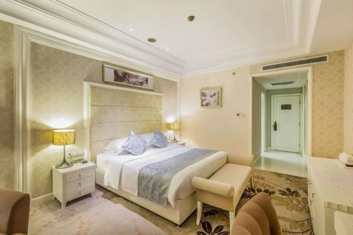A bedroom with a large bed, bedside tables, a bench, and a door leading to another room.