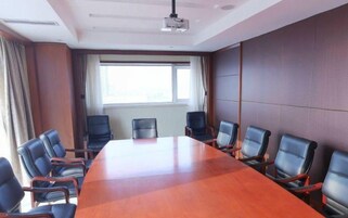 Un salón de conferencias con una mesa larga y seis sillas, un proyector y un ventanal con cortinas.