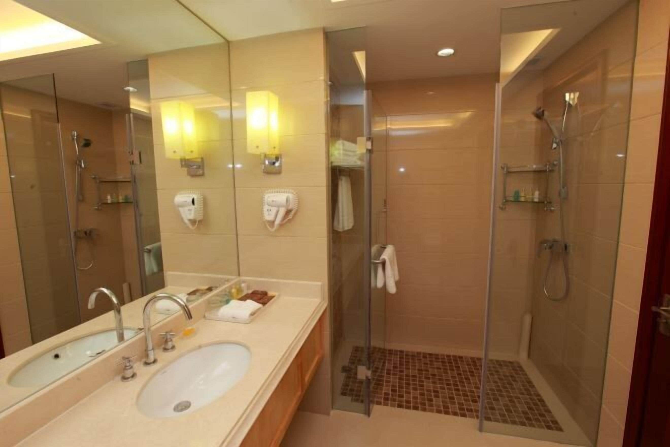 Un baño moderno con un espejo grande, lavamanos dobles, cabina de ducha de vidrio y suelo de ducha con azulejos.