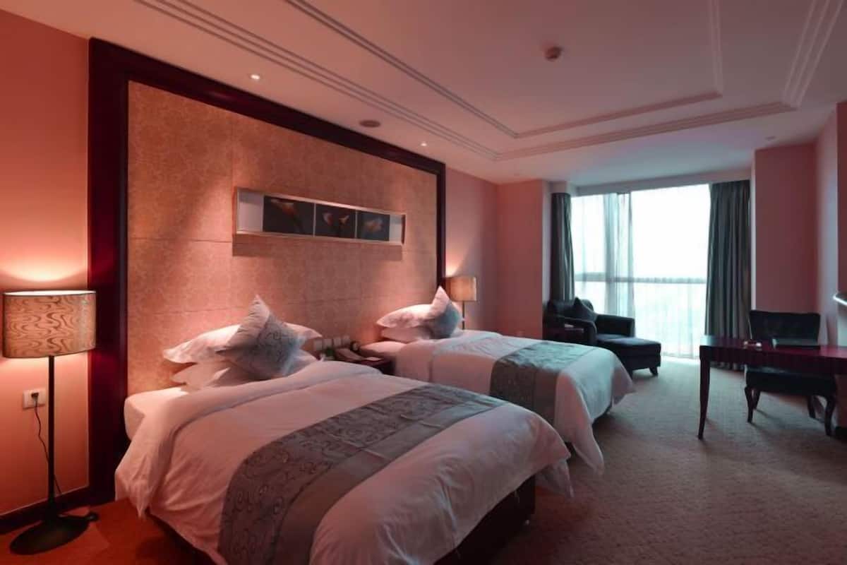 A hotel room with two beds, a desk, a chair, and a large window.