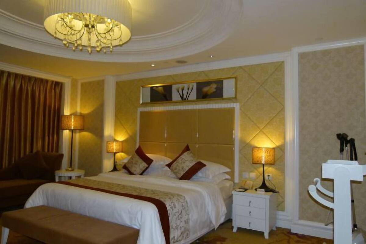 A hotel room with a large bed, bedside lamps, a small table, and a decorative wall panel.