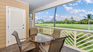 A covered outdoor area with a table and chairs, a view of a golf course, and a wooden door.