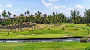 A golf course with a water hazard, palm trees, and a building in the background.