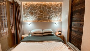 A bedroom with a stone wall headboard, a bed with white bedding, a bedside lamp, and a wooden door. - YLUNA Boutiquestay (Can Tho)