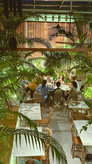 Un espacio de comedor al aire libre con mesas y sillas rodeado de abundante vegetación.