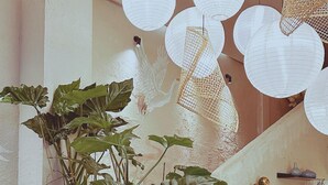A room with a staircase, a sofa, a large potted plant, hanging paper lanterns, and a wall-mounted shelf with decorative items. - YLUNA Boutiquestay (Can Tho)