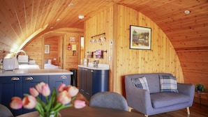 Interior acolhedor de uma cabana com paredes de madeira, uma área de jantar com mesa e cadeiras, um sofá e uma cozinha com armários e pia.