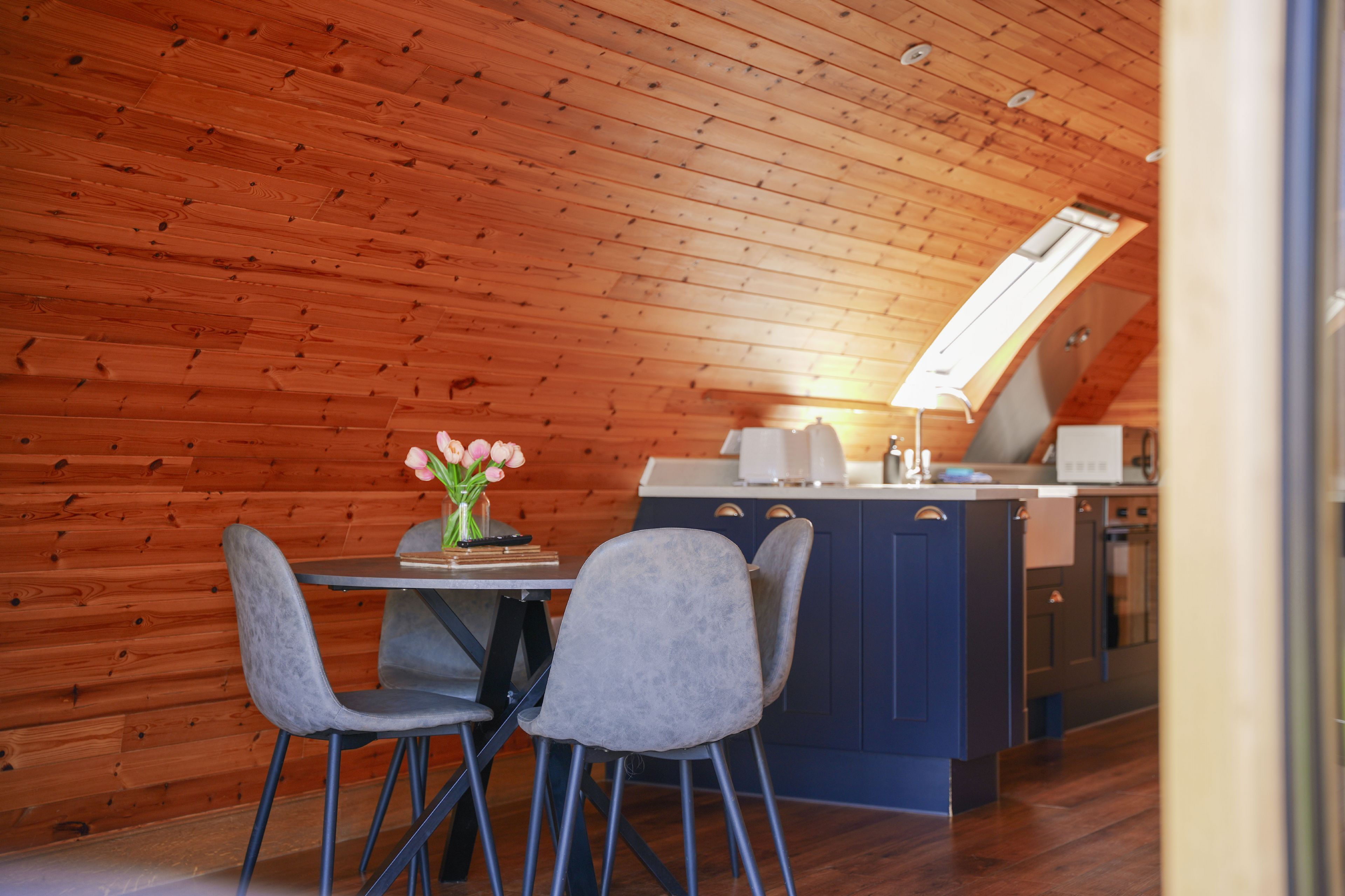A wooden-paneled room with a dining table, two chairs, a kitchen area, and a skylight.