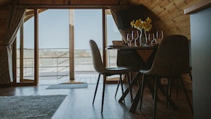 Uma área de refeições com uma mesa posta para dois, um vaso com flores amarelas e vista para o exterior através de grandes janelas.