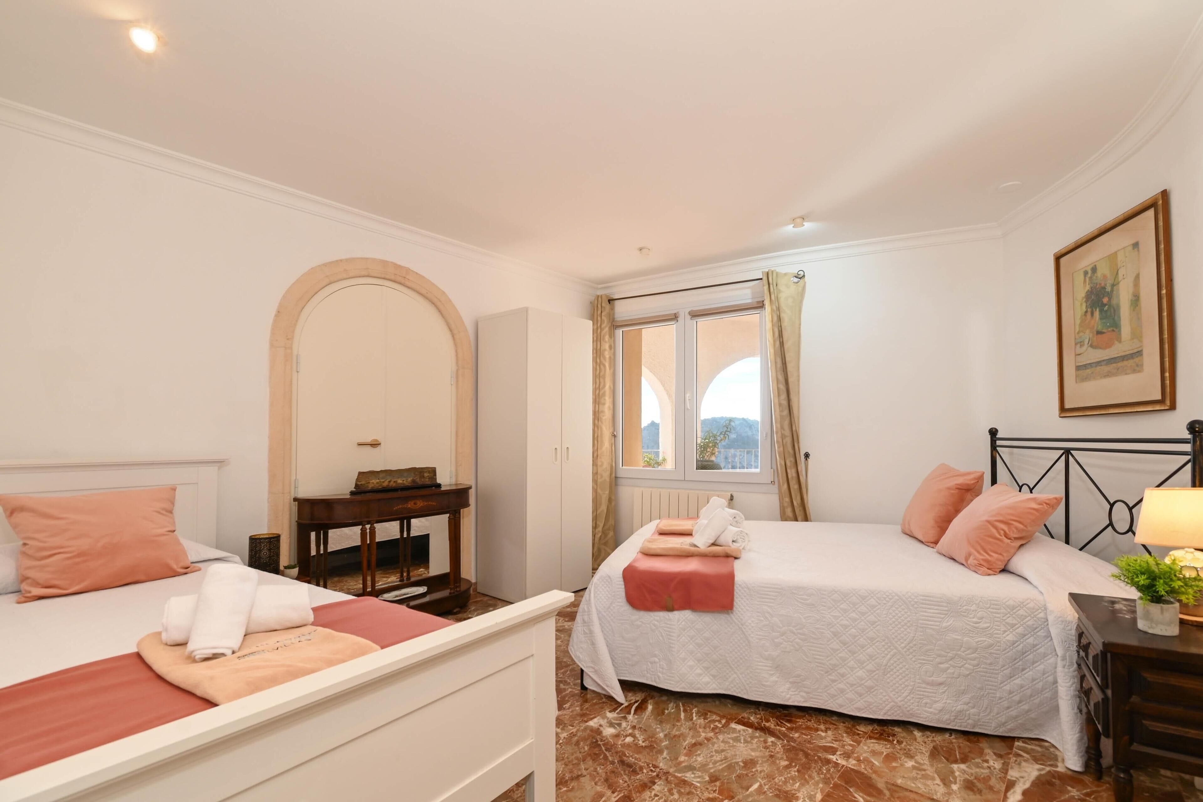 Une chambre avec deux lits, un bureau, une fenêtre avec des rideaux et un tableau encadré au mur.